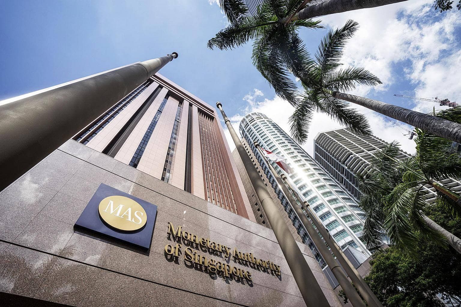 Low-angle view of the Monetary Authority of Singapore building, with its logo on the facade, surrounded by tall modern skyscrapers and palm trees under a partly cloudy sky.